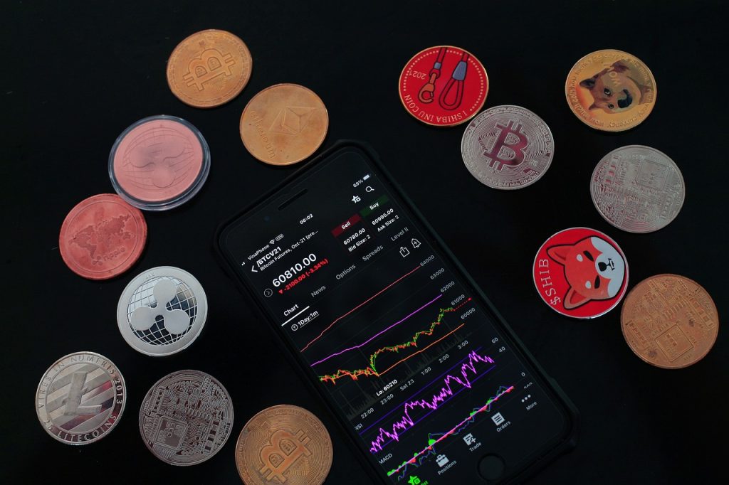 Smartphone with a cryptocurrency trading app surrounded by various crypto coins on a black surface.